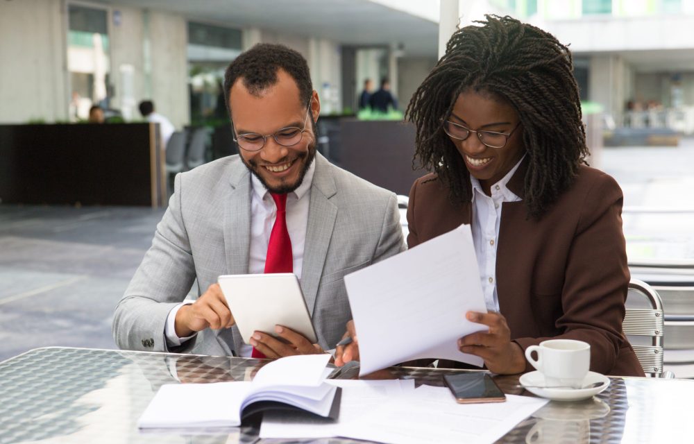Cheerful business colleagues checking documents during coffee break. Business man and woman sitting in cafe, reading documents and using tablet. Paperwork concept