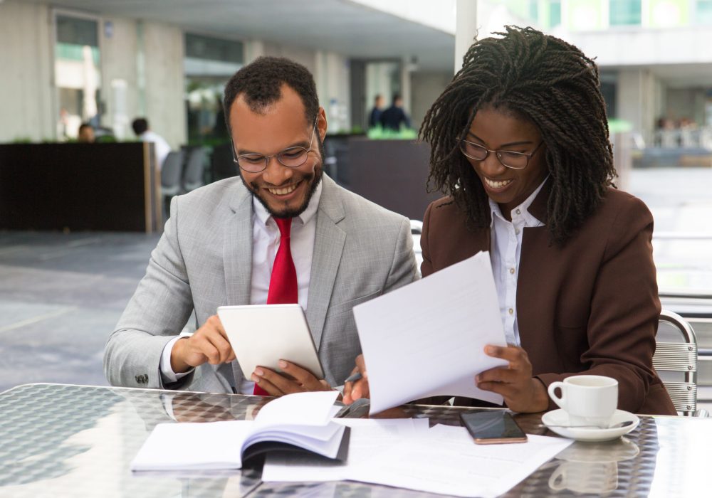 Cheerful business colleagues checking documents Cheerful business colleagues checking documents during coffee break. Business man and woman sitting in cafe, reading documents and using tablet. Paperwork concept