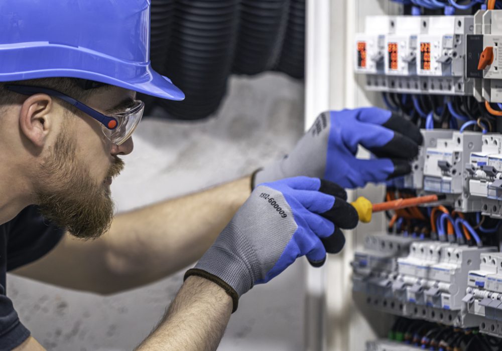 Male electrician working in a switchboard with fuses. A male electrician works in a switchboard with an electrical connecting cable.